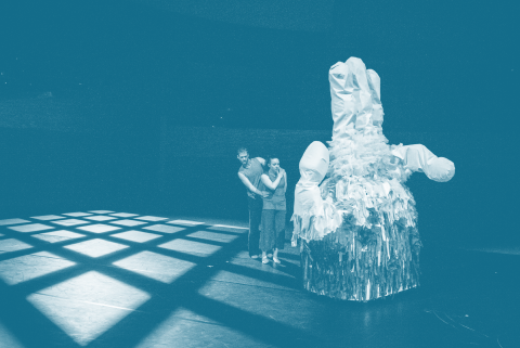 Two human dancers perform onstage with a 9 foot tall robot shaped like a hand.